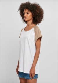 Hvit kortermet t-skjorte med beige raglanermer, avslappet passform, rund hals, laget av mykt bomullsmateriale. Sammen med denimshorts.