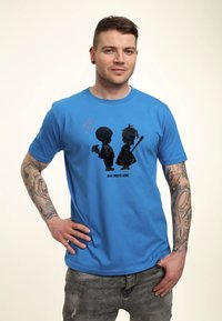 Modré bavlněné tričko s černými siluetami chlapce a dívky se srdíčky, s nápisem "CHLAPEC POTKÁ DÍVKU." Krátké rukávy, kulatý výstřih.