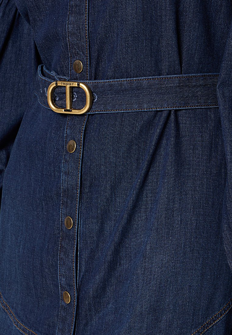 Jeansowa koszula w ciemnym niebieskim kolorze z złotym paskiem z klamrą, zatrzaskami i przeszyciami. Posiada marszczony materiał w okolicy talii.