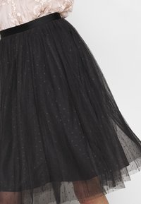 Jupe en tulle noire à coupe évasée, dotée d'une ceinture en satin et d'un motif à pois sur l'ensemble, offrant une texture en couches.