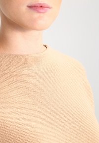 Maglione beige con un motivo di maglia testurizzato, scollo ampio e silhouette aderente, che mette in mostra una finitura di tessuto morbida e liscia.