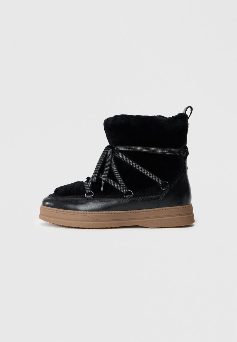 Botte d'hiver noire avec doublure en fourrure, lacets enroulés, détails en cuir et semelle en caoutchouc marron épaisse, vue de côté.