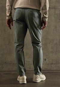 Pantalons verts à coupe fuselée, avec des poches arrière. Tissu en coton texturé et poignets côtelés complètent une tenue décontractée avec des baskets blanches.