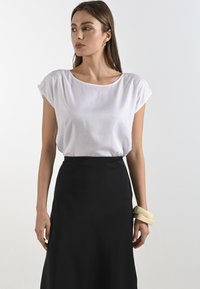 Top bianco a maniche corte con scollatura a girocollo, abbinato a una gonna nera. Presenta un tessuto liscio e un design semplice, arricchito da un bracciale crema.
