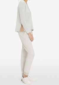 Maglia grigia chiara a maniche lunghe con fessure laterali abbinata a pantaloni grigi chiari a sigaretta e sneakers bianche con dettagli texturizzati.