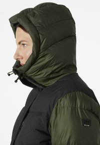 Chaqueta acolchada con cuerpo negro y capucha verde oscura. Incluye ajustadores de capucha con cordón y un logo en la manga izquierda.