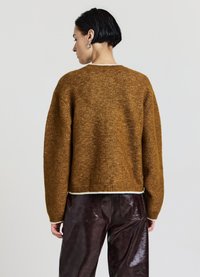 Brauner gestrickter Pullover mit strukturierter Oberfläche, geripptem Saum und weiten Ärmeln. Kombiniert mit glänzenden dunkelbraunen Lederhosen.
