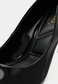 Décolleté in vernice nera con tacco alto e punta affilata, dotato di un interno imbottito, caratterizzato da una finitura lucida e un design minimalista.