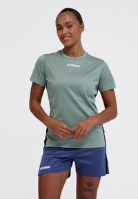 Light green short-sleeve athletic shirt with white logo, paired with blue shorts. Both garments feature a smooth texture and sport design.