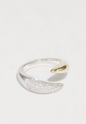 Sudraba gredzens ar izliekta dizaina; viena puse ir gluda zelta tonī, bet otra puse ir dekorēta ar strukturētām caurspīdīgām akmeņiem, radot mirdzošu efektu.