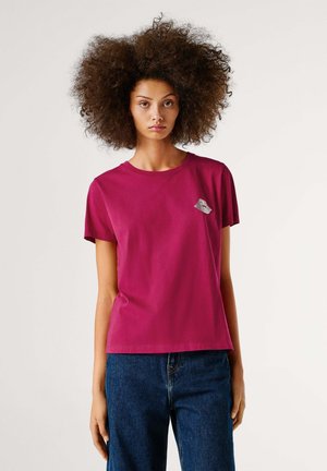Magenta katoenen t-shirt met korte mouwen en ronde hals, met een kleine grijze graphic op de linkerborst. Draagt het met donkerblauwe jeans.