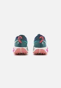 Chaussures de sport avec une tige en mesh vert sarcelle foncé, des accents roses, et une semelle texturée à pois multicolores. Conçues pour la durabilité et l'adhérence.