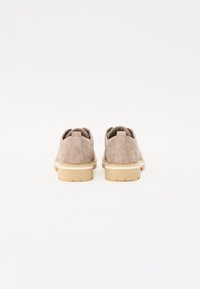 Suede beige shoes with a heel, featuring a cream-colored rubber sole, rounded toe, and a minimalist design with no visible accents.