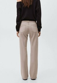 Jeans beige de tiro alto y pierna ancha con una textura suave, que presentan bolsillos y un detalle de trabilla a juego, diseñados para un ajuste casual.