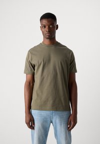 Olive green cotton t-shirt, crew neck, short sleeves, relaxed fit. Worn with light blue denim jeans, displayed against a neutral background.