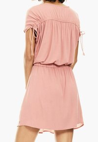 Vestido rosa de manga corta con cintura fruncida y lazos ajustables en las mangas, que presenta una tela suave y una silueta relajada.
