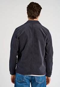 Granatowa kurtka z korduru z klasycznym kołnierzem i długimi rękawami, z centralnym szwem z tyłu, w połączeniu z niebieskimi dżinsami.