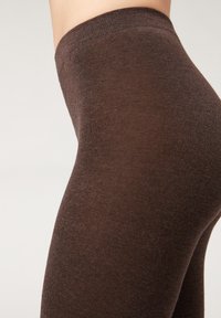 Brązowe legginsy wykonane z miękkiego, elastycznego materiału, z gładką teksturą i wysokim stanem, który dopasowuje się do ciała.