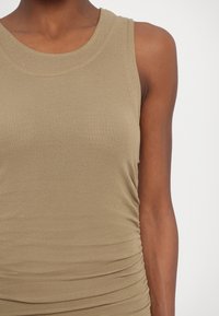 Kaki bešvarkis marškinėliai su apvaliu kaklu, minkšta tekstūra ir surinkimu šone, suteikiančiu prigludusį siluetą.