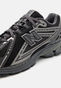 Chaussure de course New Balance noire et grise en tissu mesh, semelle épaisse, couture détaillée et logo "Nlock" sur le côté.