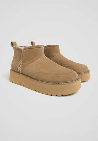 Bottines en suède brun avec une semelle à plateforme épaisse et des panneaux latéraux élastiques ; présentent des détails cousus et des languettes pour un enfilage facile.