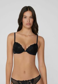 Schwarzer Spitzen-BH mit tiefem Ausschnitt und verstellbaren Trägern. Mit floralen Mustern, weicher Fütterung und einer strukturierten Form für Unterstützung.
