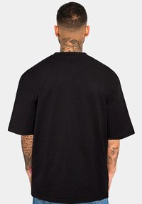 Schwarzes T-Shirt mit kurzen Ärmeln und relaxed Fit, aus Baumwolle, mit einem Rundhalsausschnitt und strukturiertem Stoff. Sichtbares Etikett an der Seite.