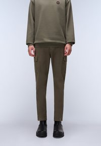 Olivengrønt sweatshirts med rund hals; matchende cargo-bukser med sidelommer; båret med sorte ankelstøvler; glat tekstur, moderne pasform.