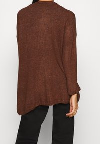 Brauner Strickpullover mit einem lockeren Schnitt, langen Ärmeln und einem gerippten Saum. Weiche Textur und eine leicht asymmetrische Länge hinten.
