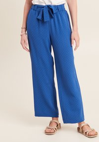 Pantaloni larghi blu con un motivo testurizzato, dotati di vita con laccetto e cuciture laterali. Abbinati a sandali color beige.
