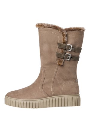 Botte en daim beige avec une bordure en fausse fourrure sur le dessus, deux sangles décoratives et des boucles en métal. Caractérisée par une semelle en caoutchouc texturée et striée.