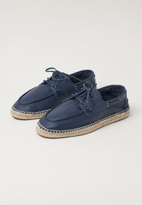 Zapatos de barco de piel azul marino con suelas de yute al estilo espadrille, que presentan cierre de cordones y ojales de metal, textura suave y diseño de puntera redondeada.