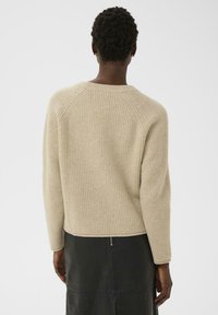 Pull en tricot côtelé beige avec un large col rond et des épaules tombantes, associé à une jupe en cuir noir avec un détail de fermeture éclair visible.