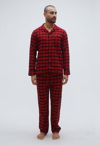 Czerwono-czarny, kraciasty zestaw piżamowy wykonany z miękkiego materiału, składający się z koszuli na guziki z kieszonką oraz dopasowanych spodni.