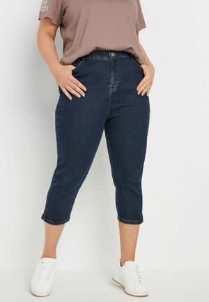 Tumma siniset capri-farkut, jotka on valmistettu denimmateriosta ja joissa on istuva malli sekä reunanompeleet. Yhdistetty neutraalinruskean t-paidan ja valkoisten tennareiden kanssa.