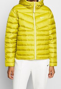 Limevihreä toppatakki hupulla, jossa on tikattu pinta, etuvetoketju ja pieni valkoinen logo vasemmassa rinnassa.