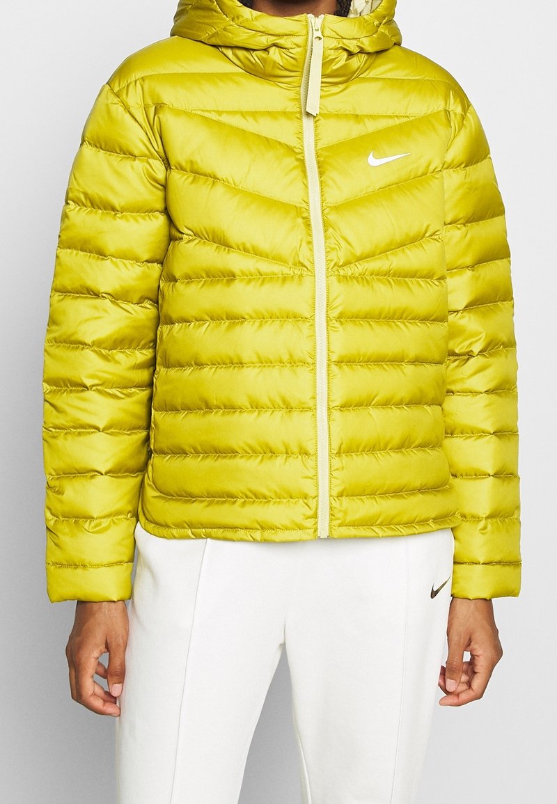 Limevihreä toppatakki hupulla, jossa on tikattu pinta, etuvetoketju ja pieni valkoinen logo vasemmassa rinnassa.