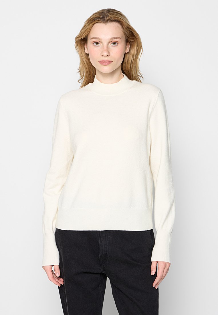 Cremfarbener Pullover mit hohem Kragen und langen Ärmeln. Die Textur wirkt weich und leicht strukturiert, mit einer lockeren Passform und geripptem Saum.