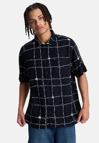 Μαύρο κοντομάνικο πουκάμισο με λευκό μοτίβο πλέγματος, κουμπιά στο εμπρός μέρος και μία τσέπη στο στήθος, κατασκευασμένο από ελαφρύ ύφασμα.