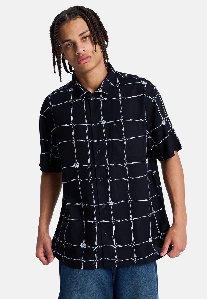 Μαύρο κοντομάνικο πουκάμισο με λευκό μοτίβο πλέγματος, κουμπιά στο εμπρός μέρος και μία τσέπη στο στήθος, κατασκευασμένο από ελαφρύ ύφασμα.