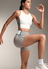 Fehér sport crop top szürke díszítéssel, türkiz varrással. Szürke kompressziós rövidnadrággal párosítva, mindkettő rugalmas anyagból készült.