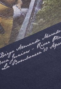 Camiseta navy con un gráfico desgastado que representa una escena de fútbol, con texto en cursiva blanca que detalla eventos y nombres de jugadores debajo de la imagen.