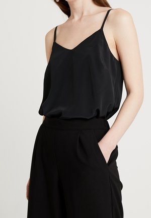 Sort satin camisolletop med V-hals og tynde stropper, med en løs pasform der falder blødt. Kombineret med sorte bukser med høj talje.