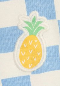 Sininen ja valkoinen ruudullinen kangas, jossa on ommeltu keltainen ananasmerkki vihreillä lehdillä, esittelee tekstuurisen suunnittelun.