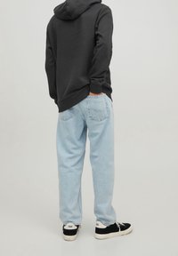 Schwarzer Kapuzenpulli mit einer Fronttasche, hellblaue, locker sitzende Jeans und schwarze Sneakers mit weißen Sohlen. Einfaches und lässiges Outfit.