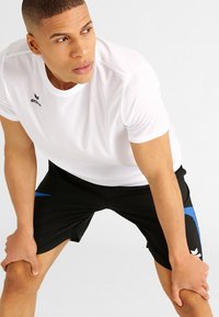 Witte sport T-shirt met een ronde halslijn, gecombineerd met zwarte shorts met blauwe zijkanten en een geborduurd logo.