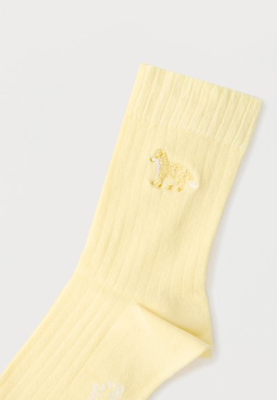Φωτεινό κίτρινο ριμπ κάλτσα με μικρό κεντημένο σκύλο ράτσας χρυσός ριτρίβερ κοντά στη μανσέτα σε λευκό φόντο.