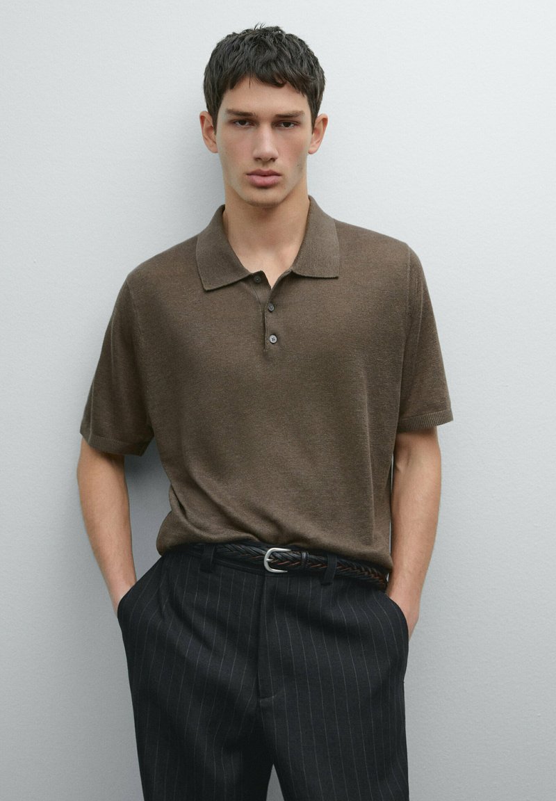 Hnědé polo tričko s krátkým rukávem a třemi knoflíky, spárované s černými kalhotami s proužky a tkaným opaskem, na neutrálním pozadí.