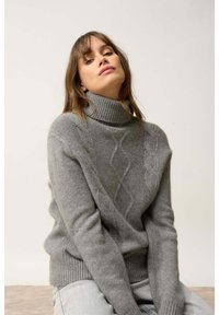 Szary sweter z golfem, wykonany z miękkiej dzianiny, z motywem warkocza i prążkowanym dołem, noszony z jasnymi dżinsami.