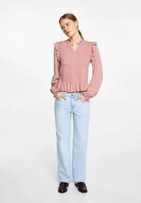 Dammig rosa smockad topp med volanger på axlarna, V-ringning och utsvängd nederkant. Matchas med ljusblå raka jeans och svarta skor.